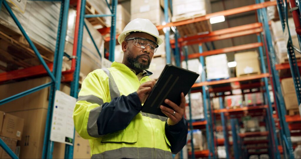 Warehouse, black man and manufacturing with tablet, inventory and checklist in a factory. African person, worker and employee with tech and inspection with digital app for logistics and online stock.